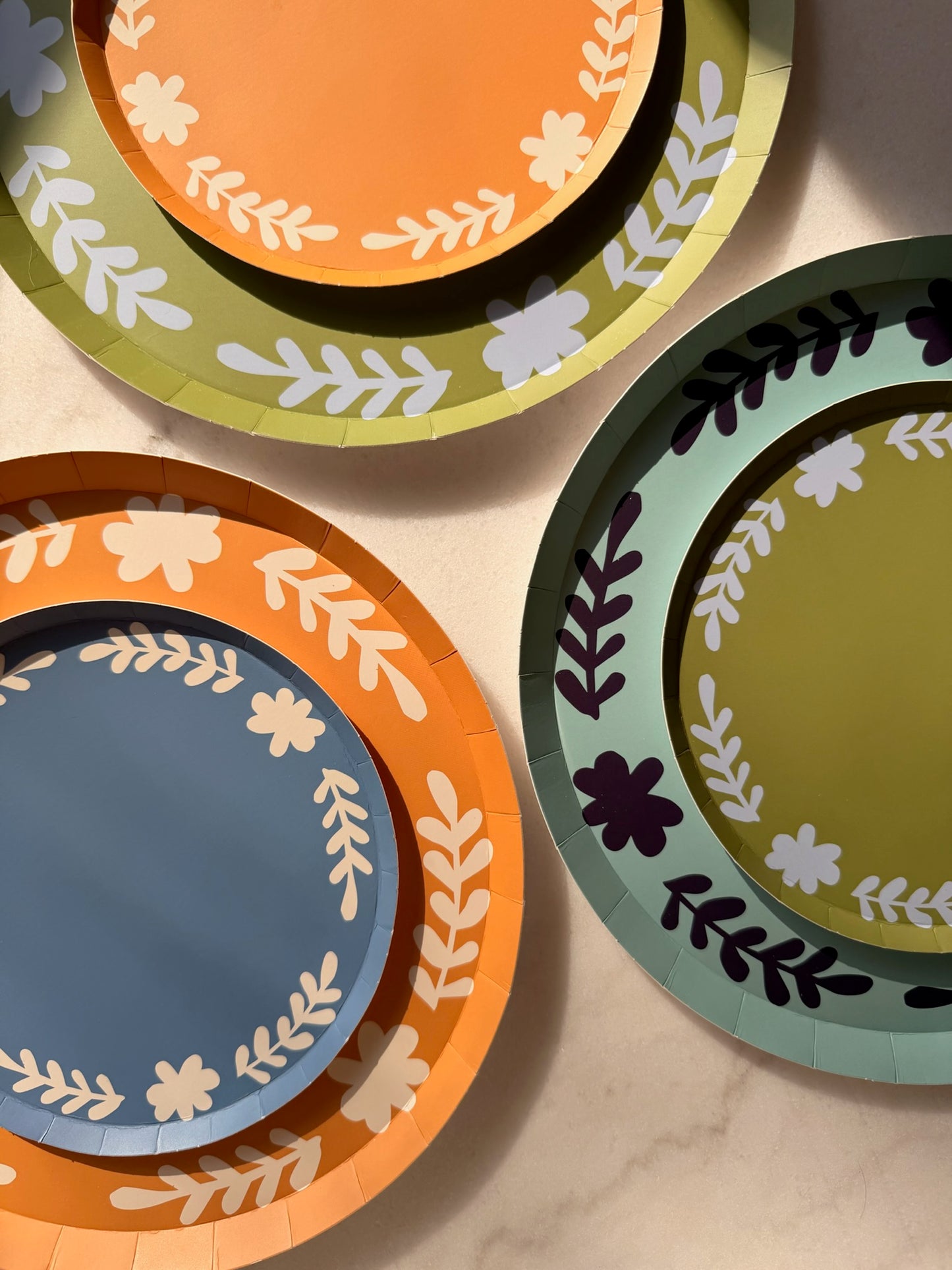 orange, blue and green colored plates with a floral boarder stacked on top of one another. 