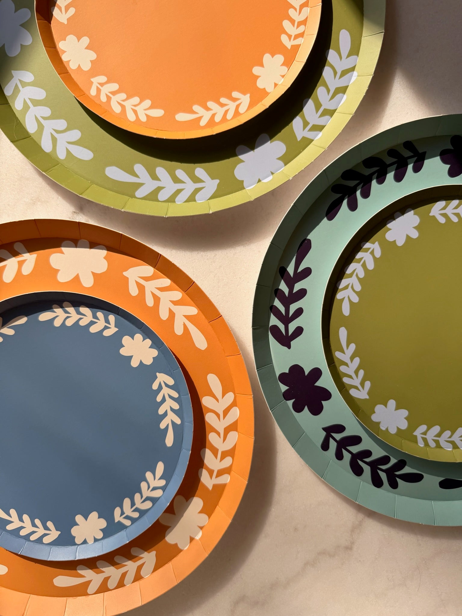 orange, blue and green colored plates with a floral boarder stacked on top of one another. 