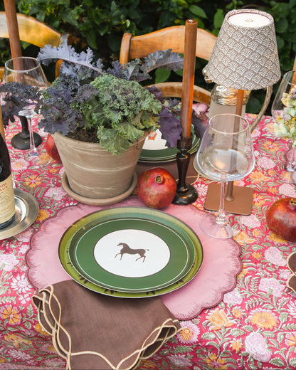 An outdoor table set with pink placemats and layered plates. The top plate has an image of a horse with a thick green border. 