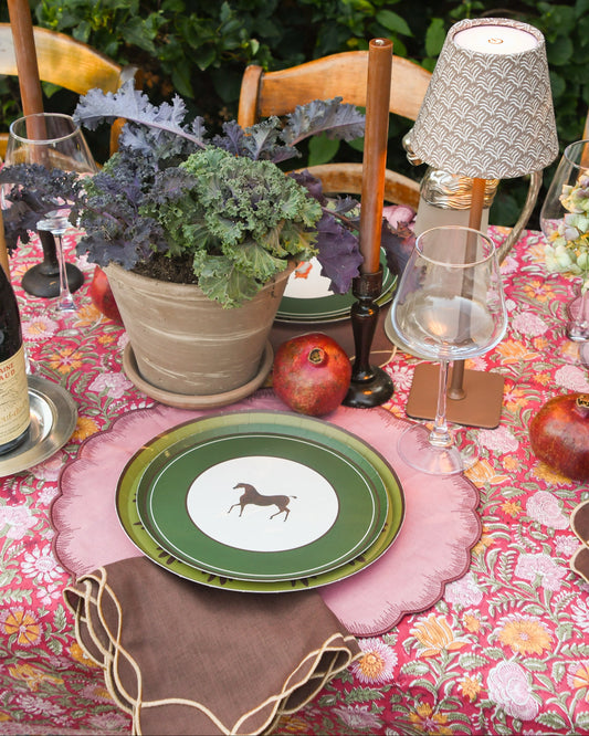 An outdoor table set with pink placemats and layered plates. The top plate has an image of a horse with a thick green border. 