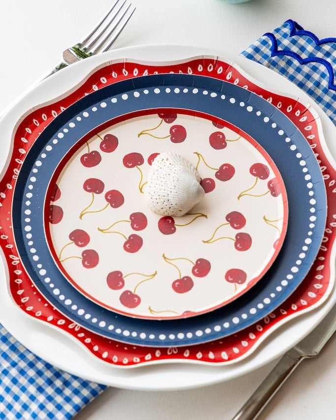 Stack of decorative plates with cherry pattern on a white tablecloth.
