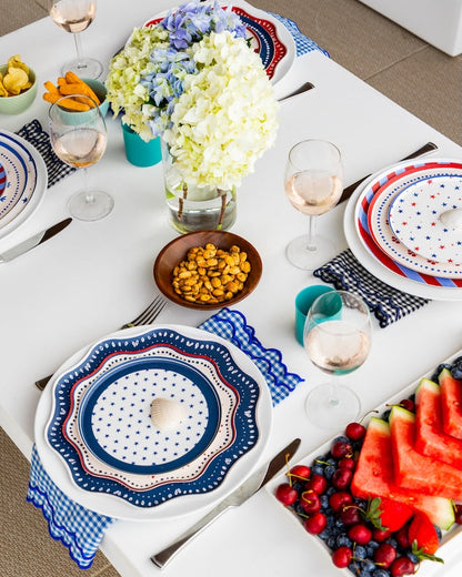 Elegant table setting with decorative plates, fruit, and flowers on a white tablecloth.