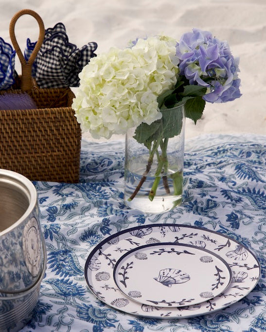 a beach setting with a patterned blanket and decorative plate.