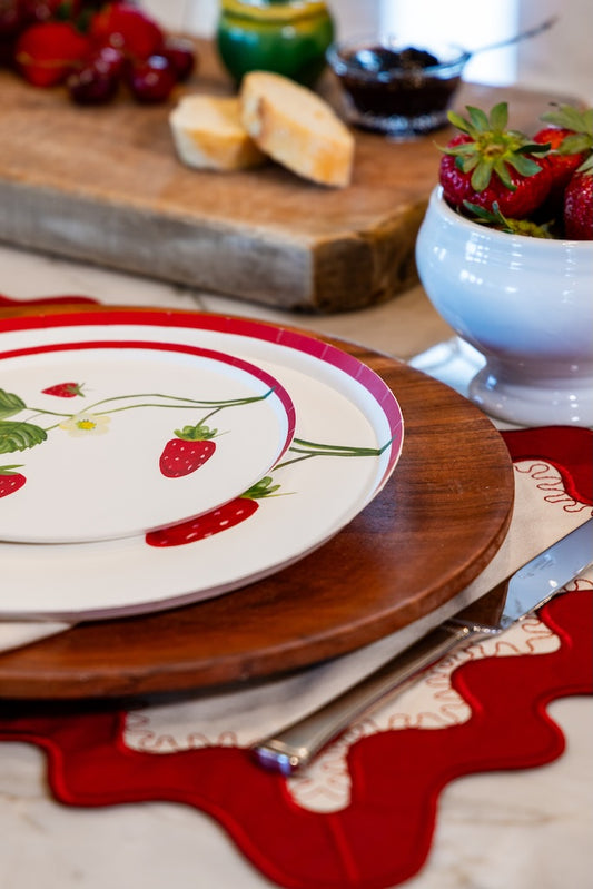 Plates with strawberries at a table setting with bread and fruit 