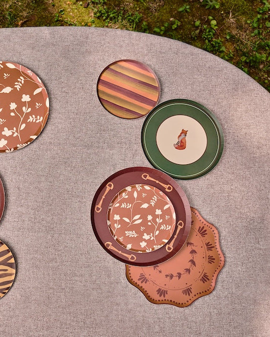 A set of decorative plates with various patterns including zebra print, floral motifs, stripes, and dog silhouettes, arranged on a round gray table outdoors.