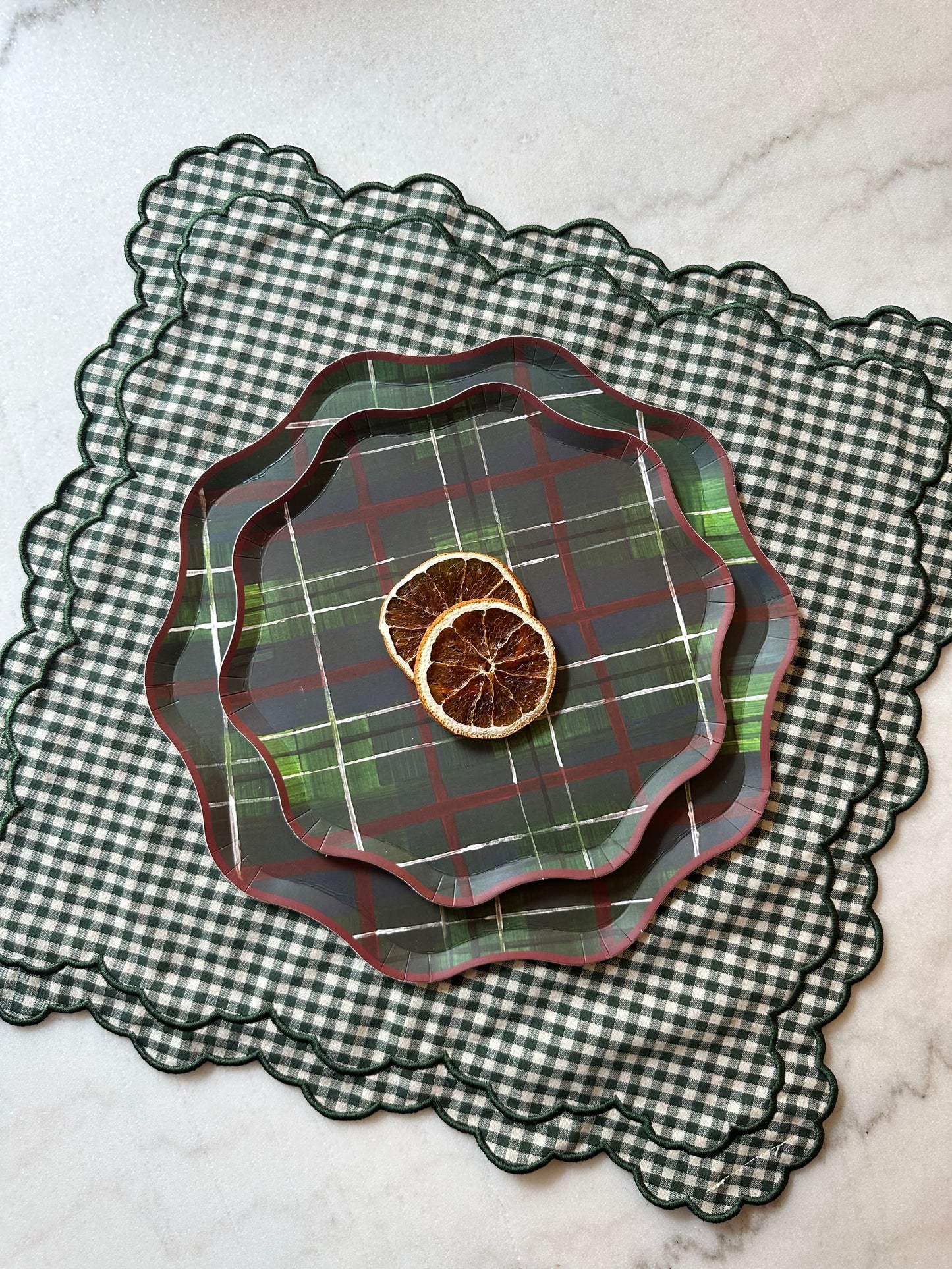 Stack of plaid  plates on a checkered placemat with dried oranges.