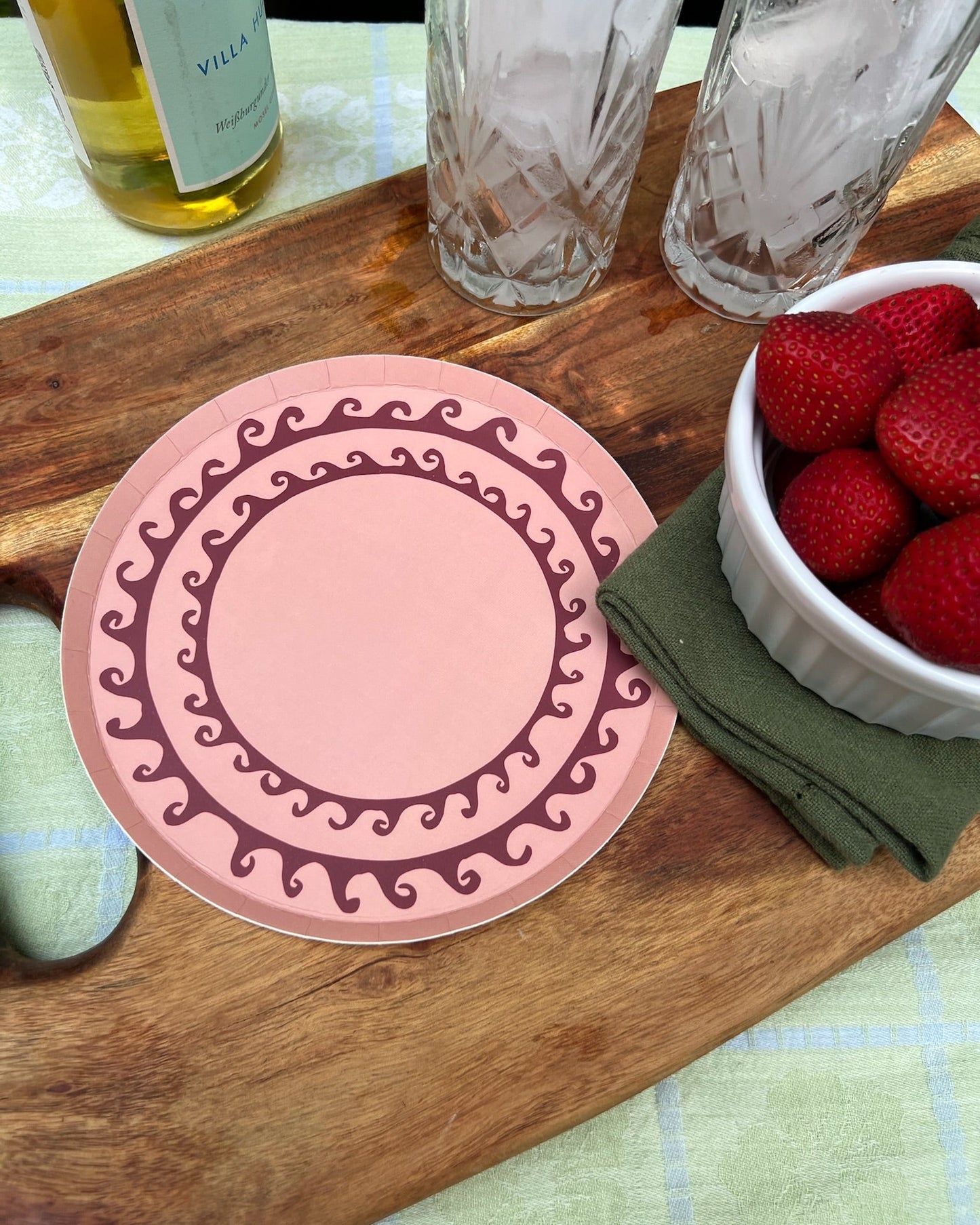 Pink plates with decorative pattern on a wooden surface with a bowl of strawberries and glasses.