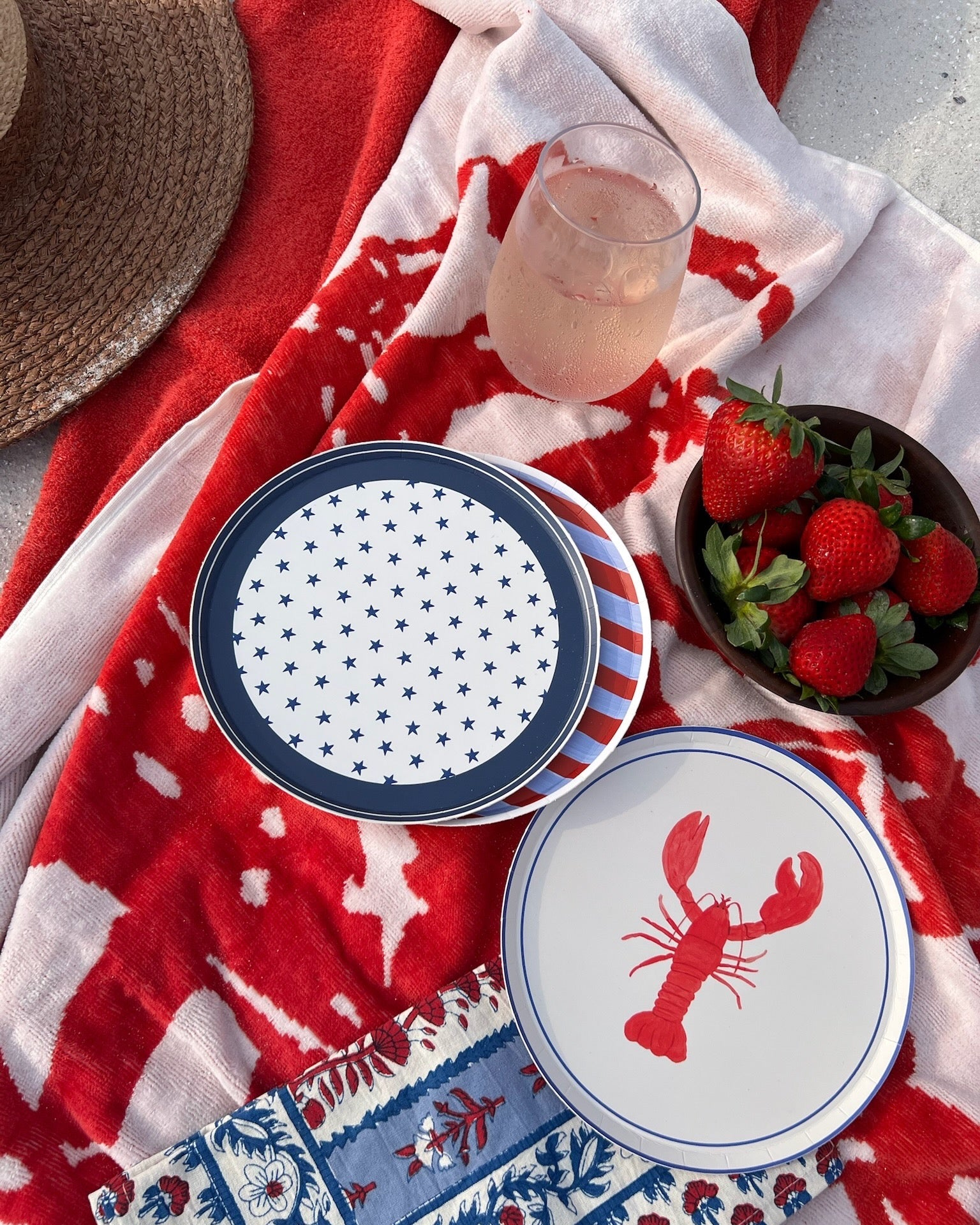 red white and blue plates set on a towel with a glass of wine and a bowl of strawberries