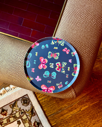 A round decorative plate with a colorful butterfly pattern on a dark blue background.