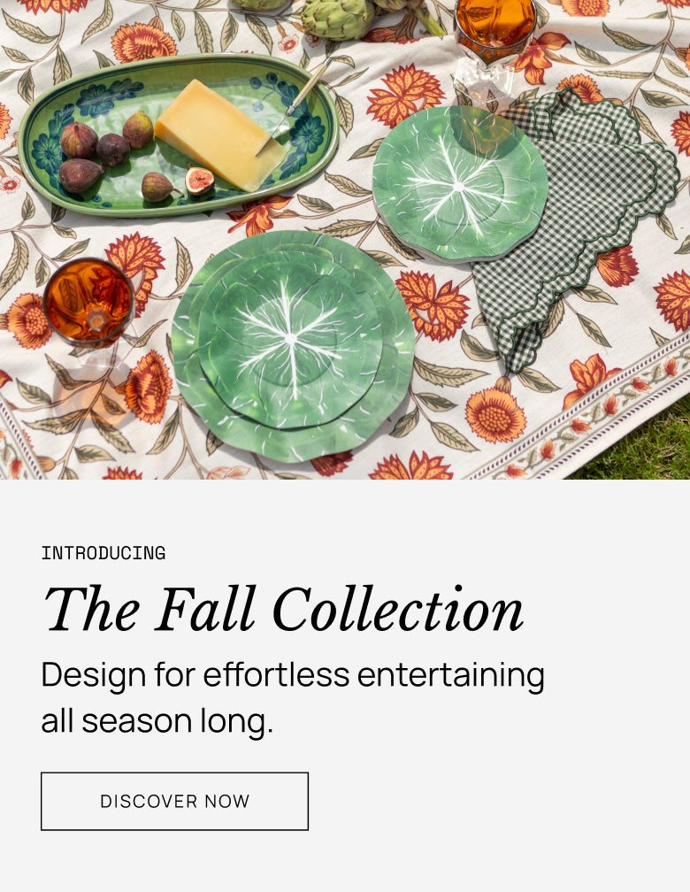 Table setting with green plates, fruit, and glasses on a patterned tablecloth with text promoting 'The Fall Collection'.