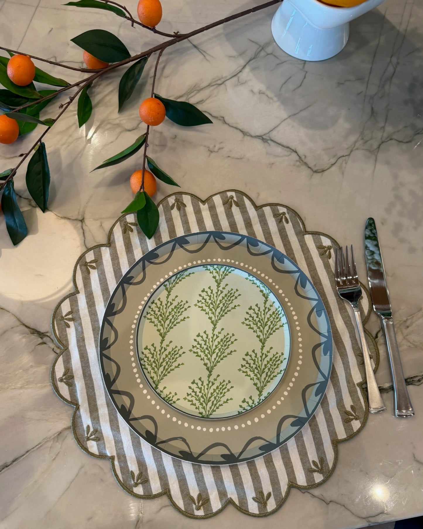 Decorative plate with floral pattern on a marble surface with cutlery and oranges.
