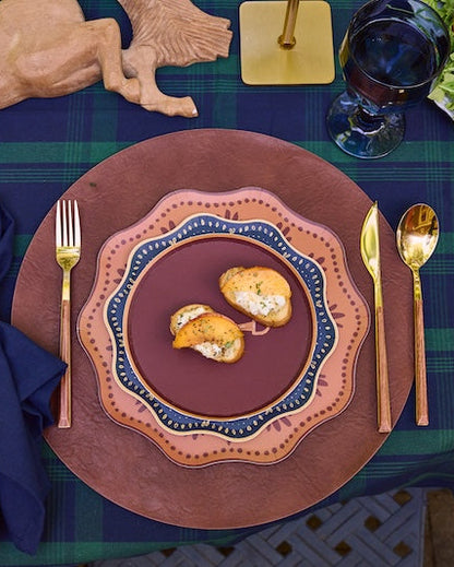 decorative plates layered on a leather charger with gold silverware and a navy napkin.
