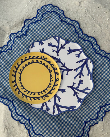 Two decorative plates on a checkered placemat in the sand