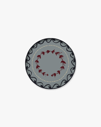 A round decorative plate with a gray center, a ring of small red floral motifs, and a dark gray outer border with black scrollwork and a dotted inner line, shown on a plain light gray background.
