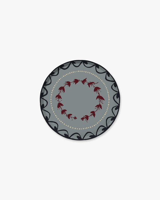 A round decorative plate with a gray center, a ring of small red floral motifs, and a dark gray outer border with black scrollwork and a dotted inner line, shown on a plain light gray background.