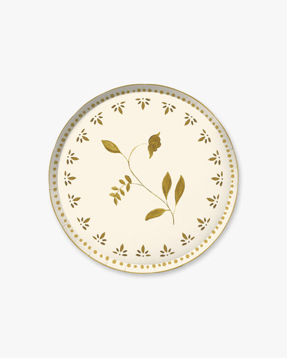 A round paper plate with a cream background, decorated with a central olive branch motif in metallic gold and a border of small gold leaf cutouts and dots, shown on a light gray background.