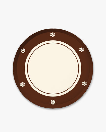 A round paper plate with a dark brown outer rim decorated with small white floral motifs, a cream-colored inner rim, and a blank cream center, shown on a light gray background.