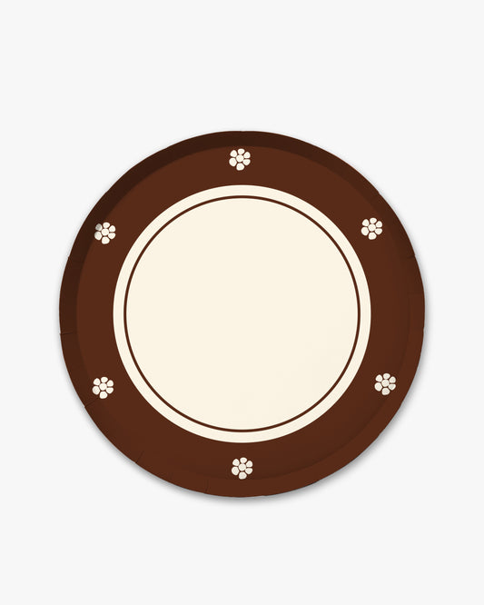 A round paper plate with a dark brown outer rim decorated with small white floral motifs, a cream-colored inner rim, and a blank cream center, shown on a light gray background.