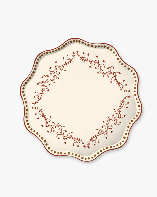 A  plate with a scalloped rim, featuring a cream-colored center and a border decorated with a reddish-brown floral vine pattern and a border of small gold dots, shown on a light gray background.