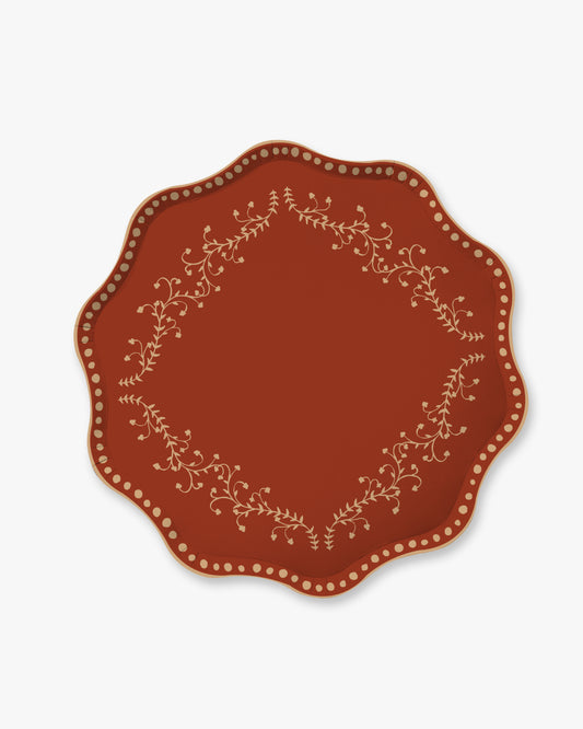 A scalloped plate in terracotta red with a delicate cream floral vine border and a ring of small cream dots around the rim, shown on a light gray background.