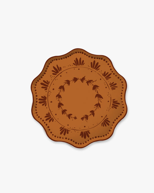 A round decorative plate with a scalloped edge, featuring a brown and terracotta orange floral pattern on a light gray background.