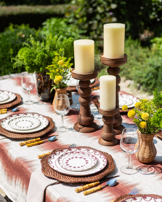 Elegant outdoor table setting with candles, plates, and flowers.