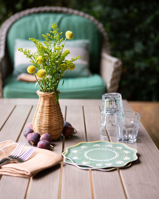 Outdoor table setting with a vase of flowers, glasses, and a plate on a wooden table.