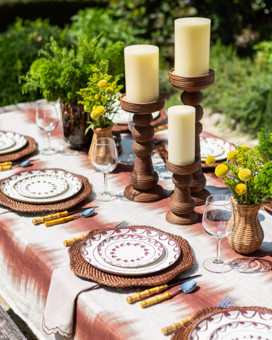 Elegant outdoor table setting with candles, plates, and flowers.