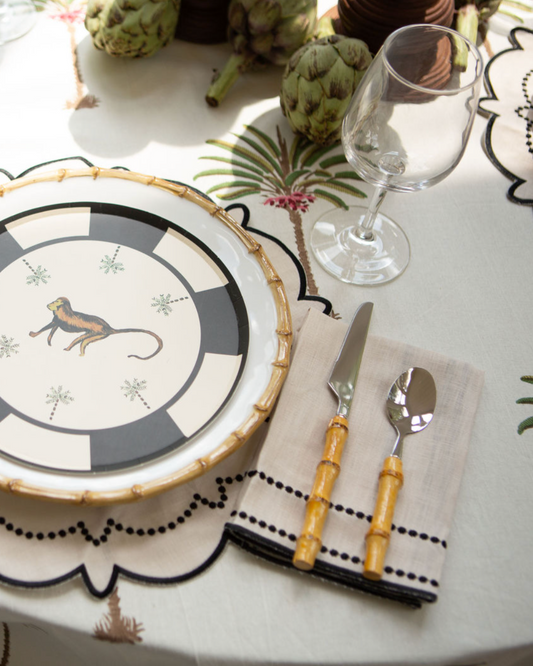 Table setting with decorative plates, cutlery, and a glass on a tablecloth with palm tree design.