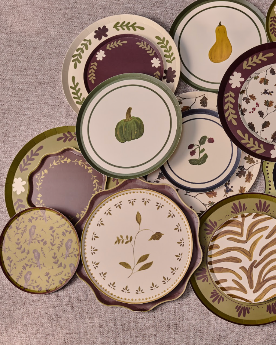 A collection of decorative plates with autumn-themed patterns, including pumpkins, gourds, leaves, and stripes, arranged on a table.