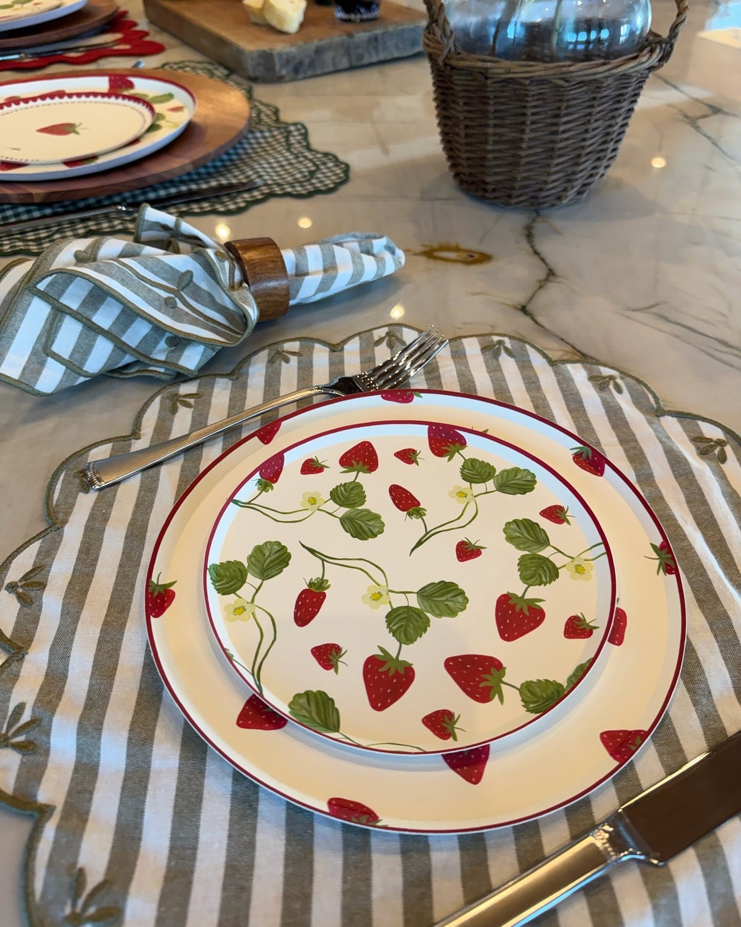 Dinner plate with strawberry pattern on a table setting with cutlery and napkins.