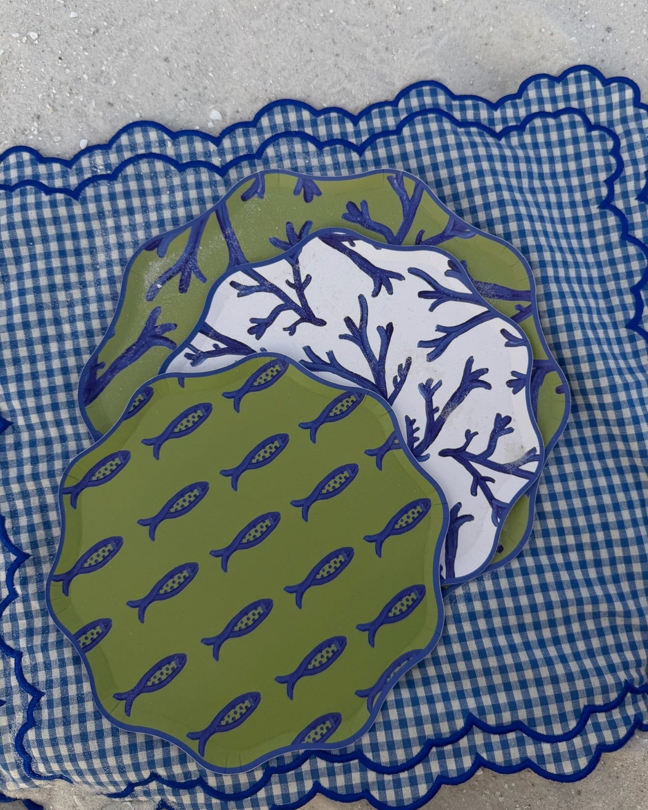 A stack of blue and green decorative plates on a checkered placemat in the sand