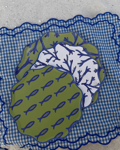 A stack of blue and green decorative plates on a checkered placemat in the sand