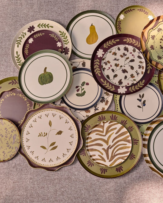 A collection of decorative plates with autumn-themed patterns, including pumpkins, gourds, leaves, and stripes, arranged on a table.