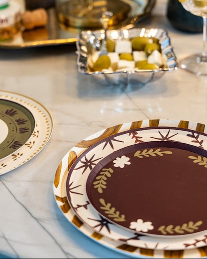 A close-up of decorative dinnerware on a marble table, featuring a round plate with a dark brown center and a gold and white floral border, stacked on another matching plate.