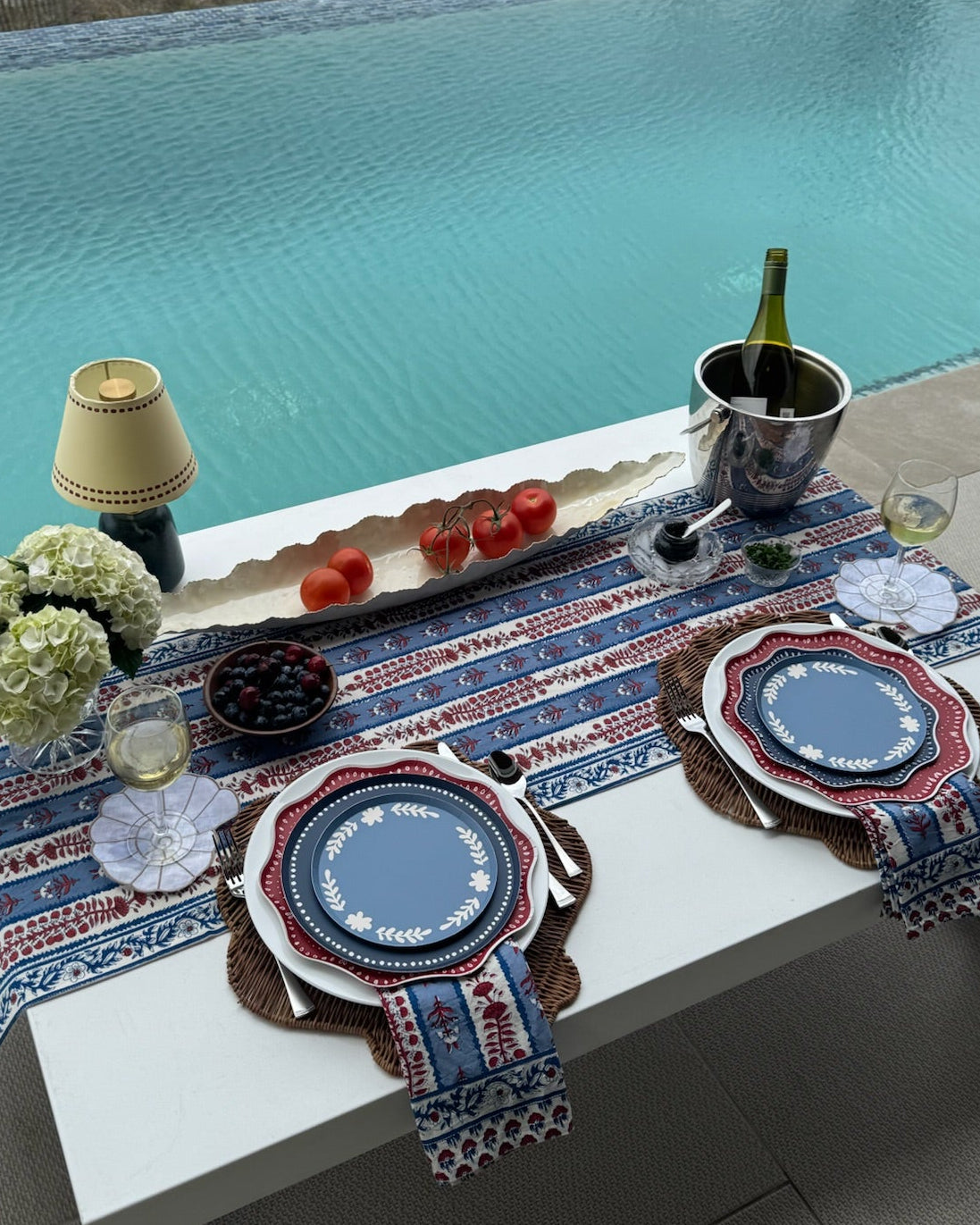 a table setting next to a pool with decorative plates and table linens