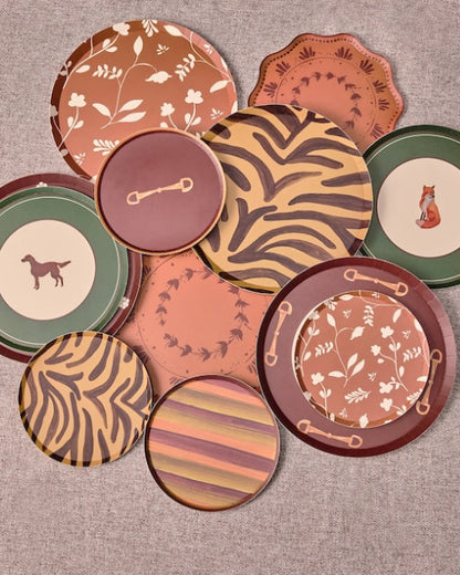 A group of decorative plates in earthy terracotta, brown, green, and beige tones, arranged on a round gray surface outdoors.