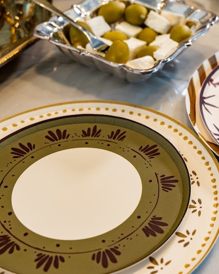 A close-up of decorative plates on a light marble tabletop, with a small dish of olives and cheese in the background.