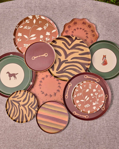 A group of decorative plates in earthy terracotta, brown, green, and beige tones, arranged on a round gray surface outdoors.