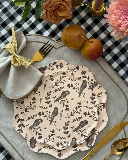 Decorative plate with bird pattern on a checkered tablecloth with flowers and cutlery.