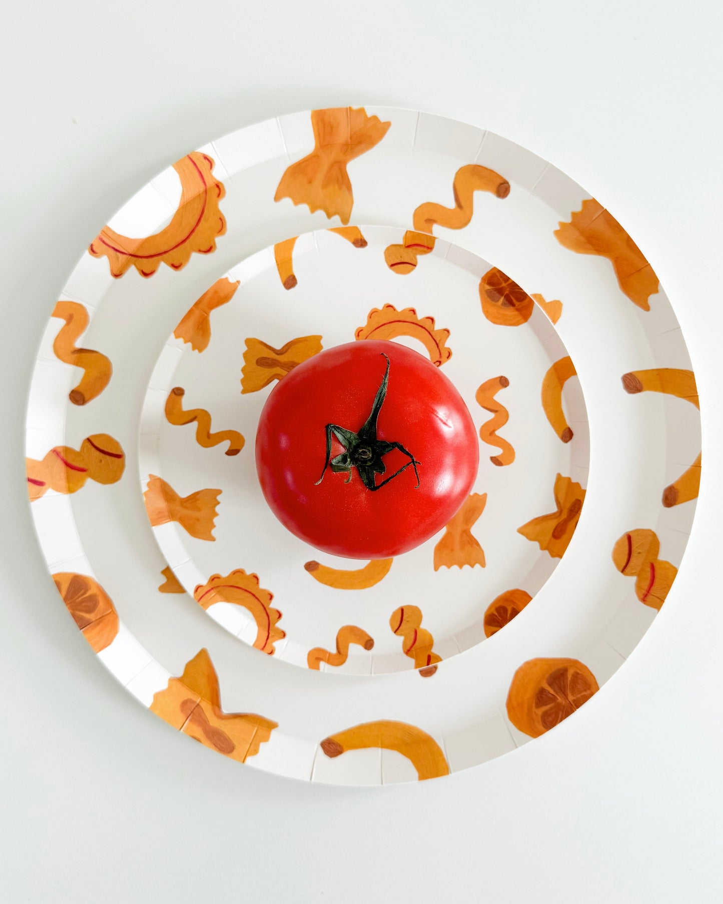 two plates stacked with pasta designs on them and a tomato on the plate