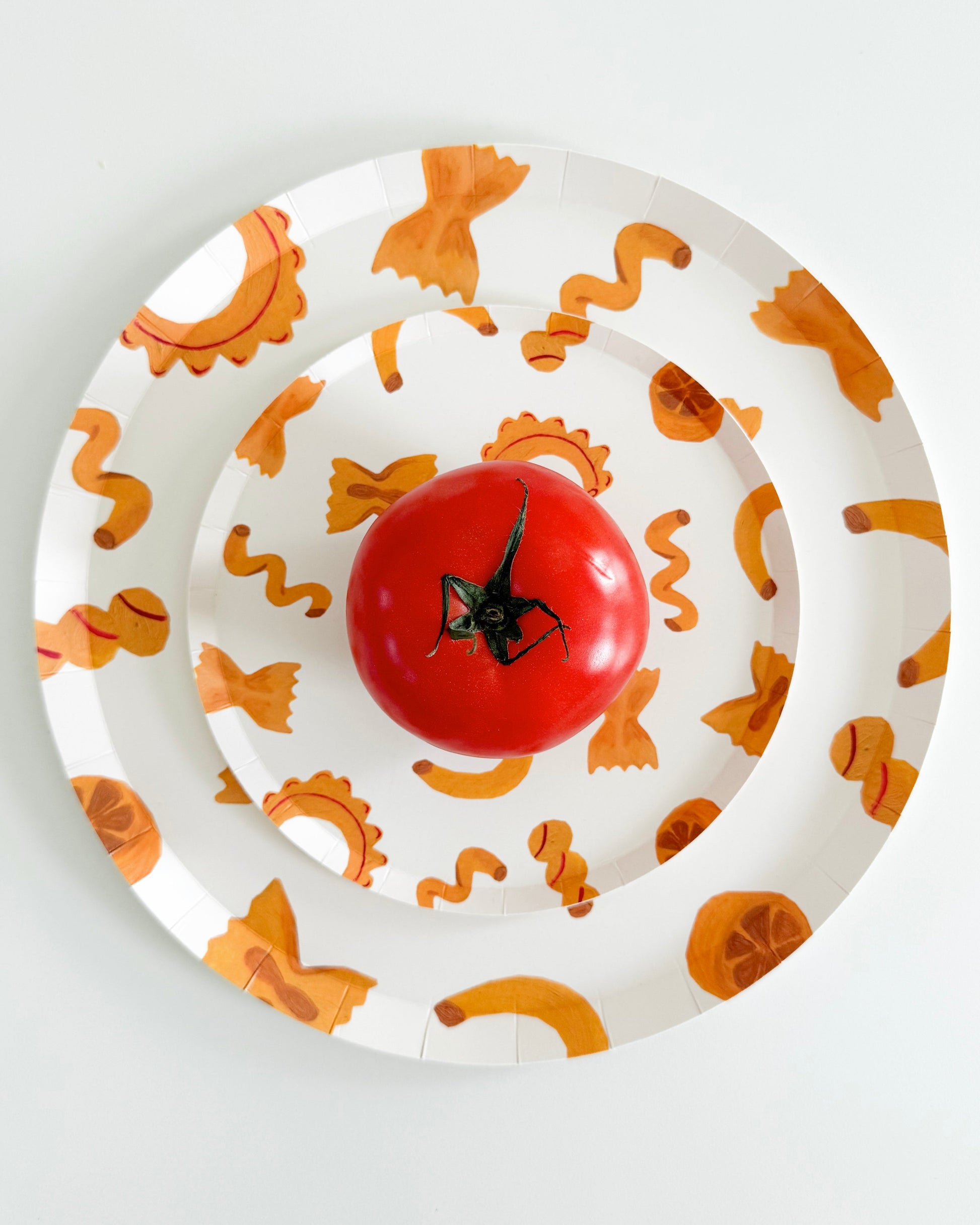 two plates stacked with pasta designs on them and a tomato on the plate