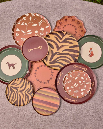 A group of decorative plates in earthy terracotta, brown, green, and beige tones, arranged on a round gray surface outdoors.