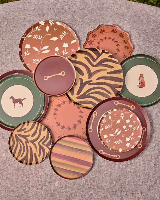A group of decorative plates in earthy terracotta, brown, green, and beige tones, arranged on a round gray surface outdoors.