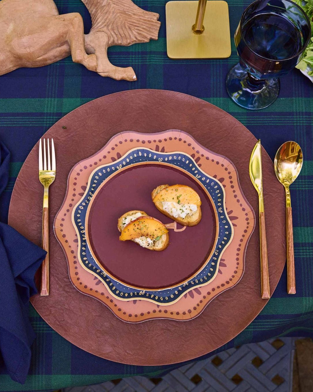 decorative plates layered on a leather charger with gold silverware and a navy napkin.