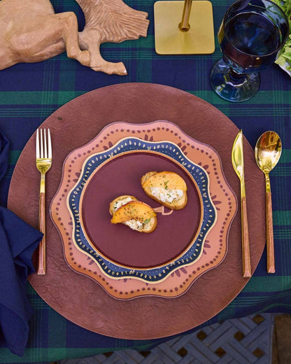 decorative plates layered on a leather charger with gold silverware and a navy napkin.