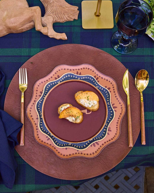 decorative plates layered on a leather charger with gold silverware and a navy napkin.